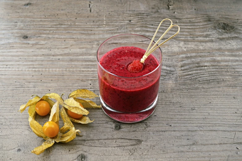 red smoothie with fresh fruit on the side, beside a pair of yellow strawberries