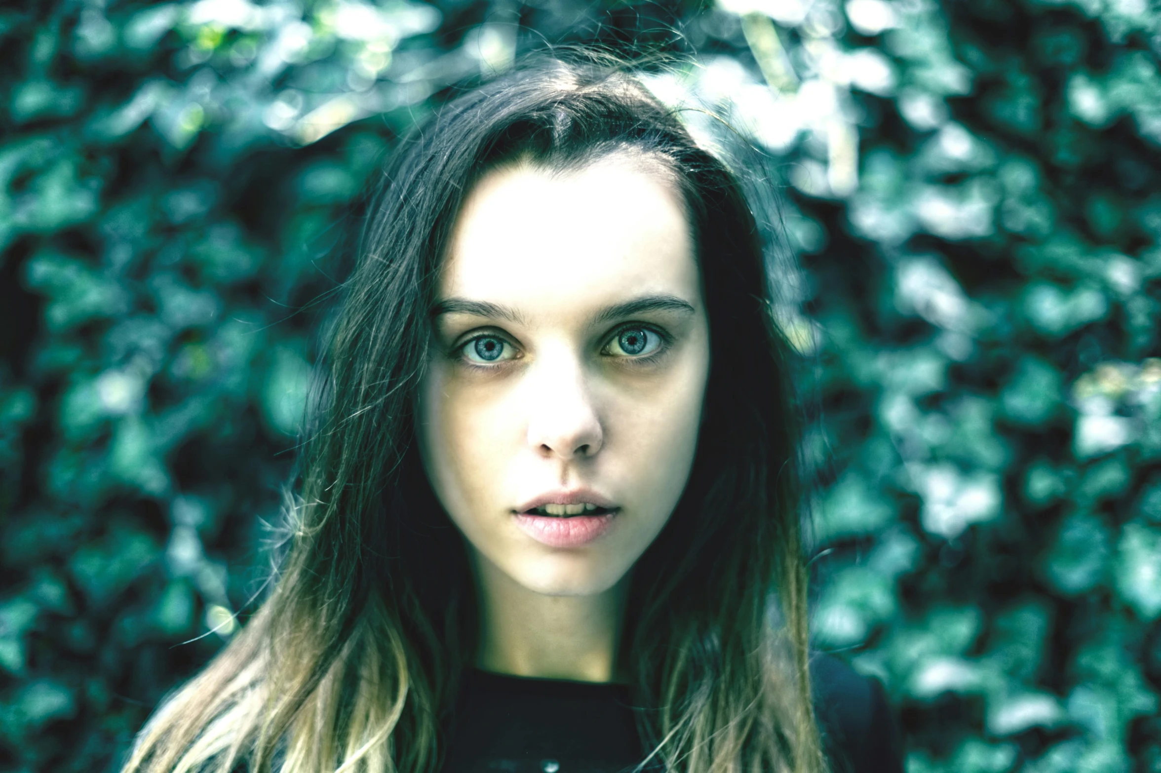 a beautiful young woman with long hair standing in front of some leaves