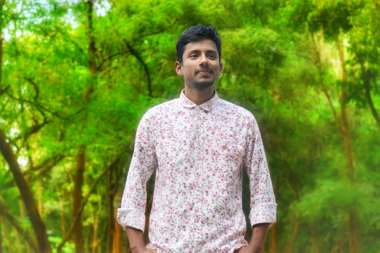 man standing near tree's in a forest wearing a pink shirt