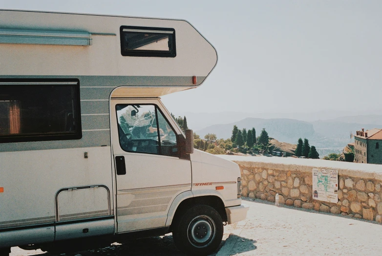 a white bus with the door open near a stone wall