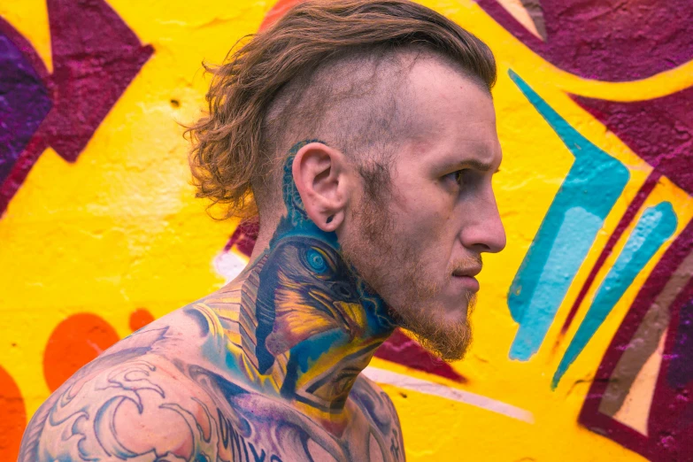 a tattooed man standing next to a colorful wall