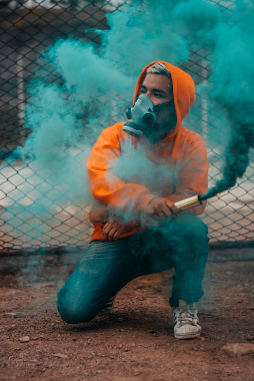the man wearing a gas mask is squatting down and holding a burning cigarette