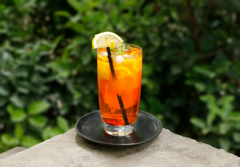 a glass with an orange drink on a plate with a drink in the foreground and another cup behind it