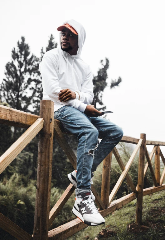 a young man sits on a fence and checks his cell phone