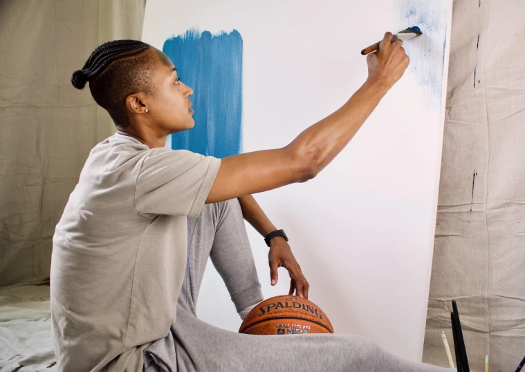 man sitting on floor painting a blue and white mural