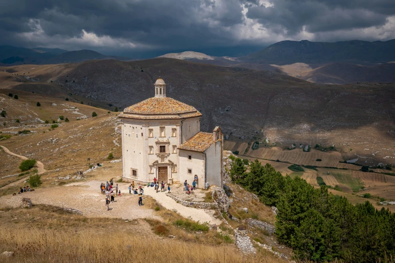 people gather at the base of a church atop a hill