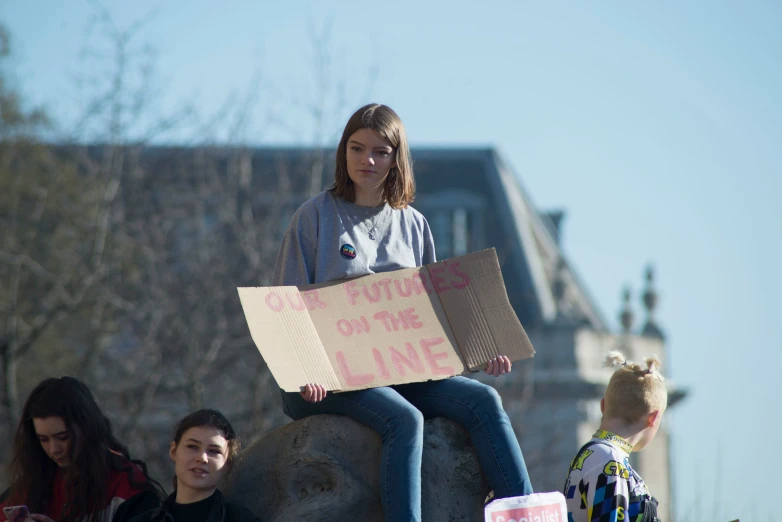 a woman sitting on a rock with a protest sign