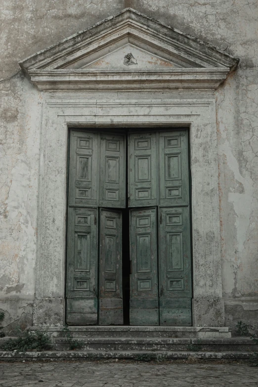 an old, crumbling building with two large green doors