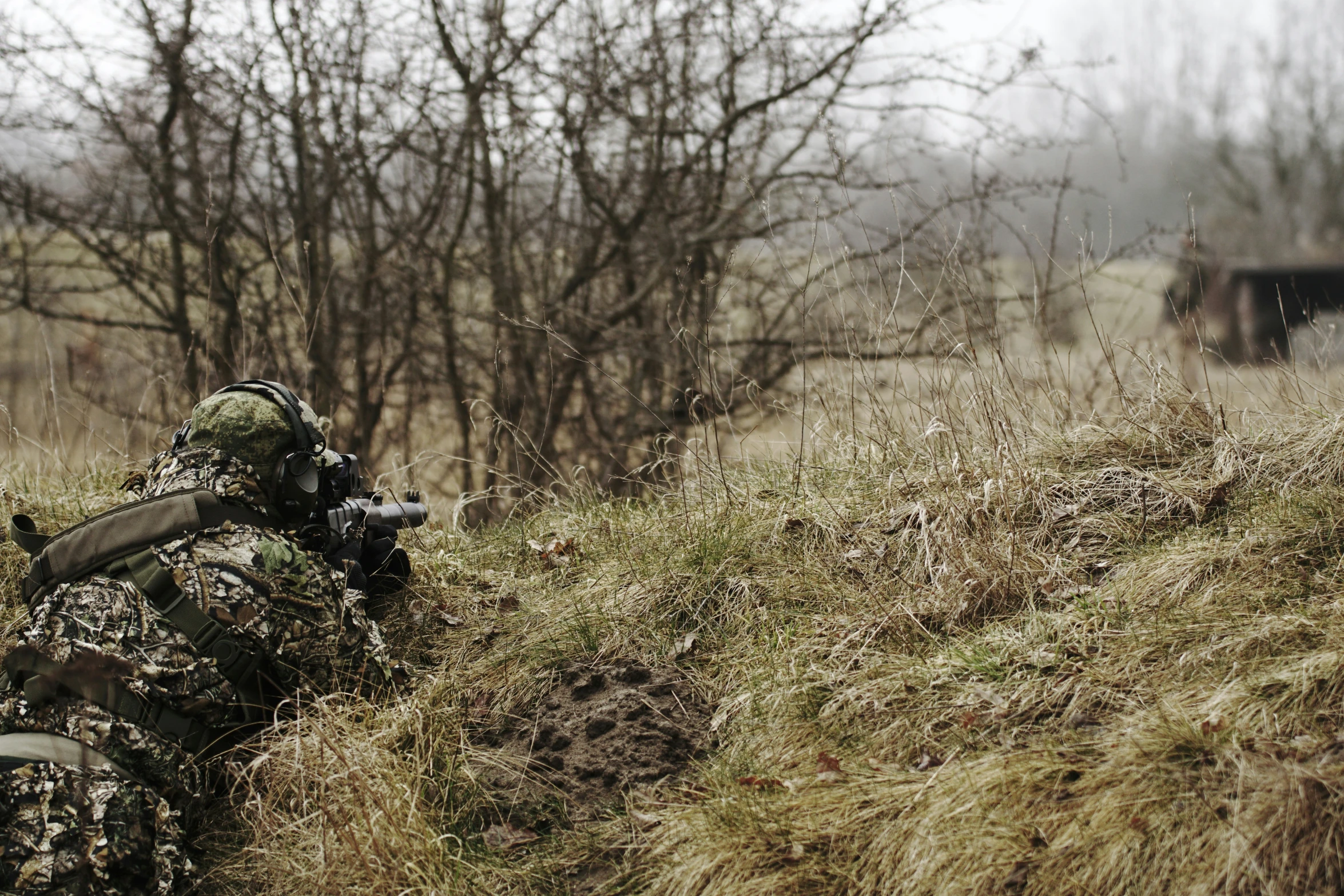 a person with a hunting scope is squatting in the grass