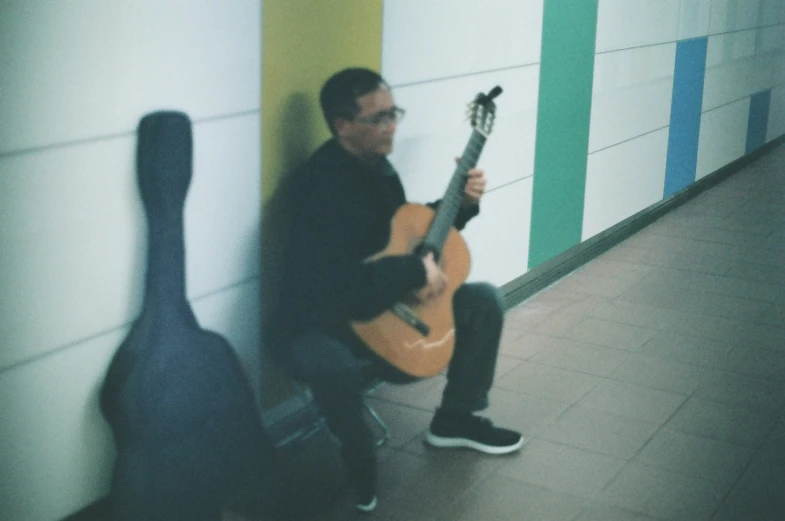 a man in a black jacket sitting down holding an acoustic guitar