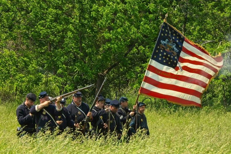 a group of men standing around a flag in tall grass