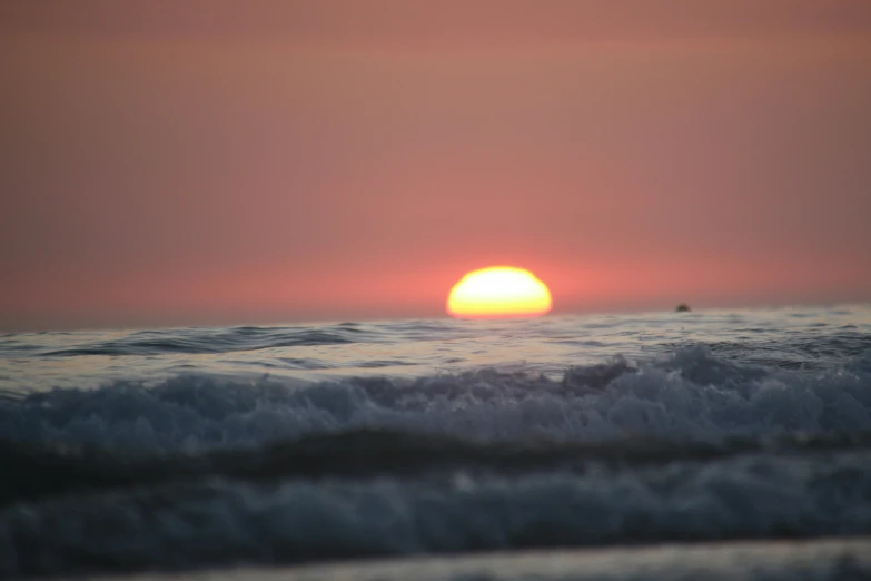 the sun rising behind a cloudy horizon in the ocean