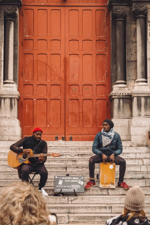 two people playing instruments sitting outside of a brown door