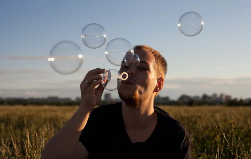 man blowing bubbles in open field with blue sky