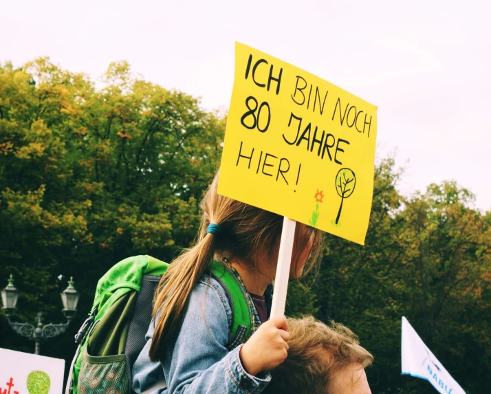 a young man holding a sign that says, i h b nggh 80 jahre here