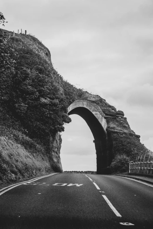 a stone arch on a country road near a hill