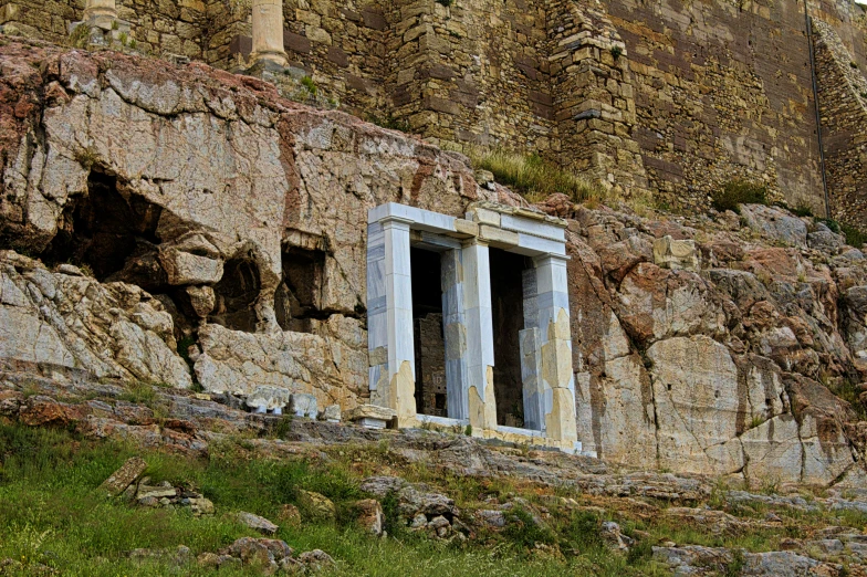 an old stone building with two windows and grass