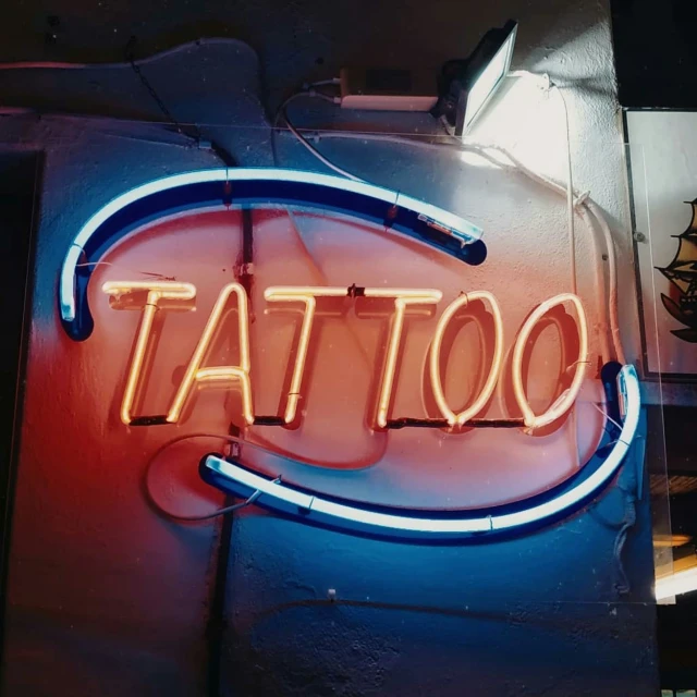 a blue neon sign reading tattoo is mounted on the wall
