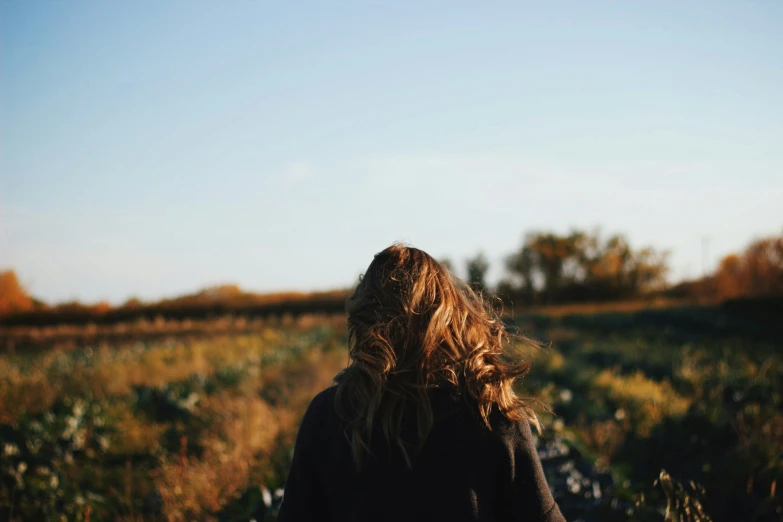 long haired woman walking on a path through grass in a field