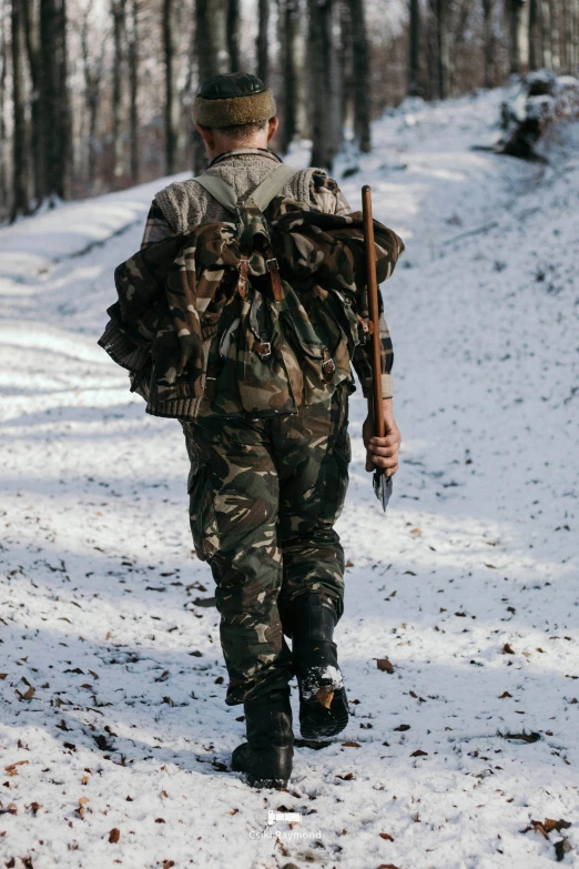 man walking down a snow covered hill holding onto a stick