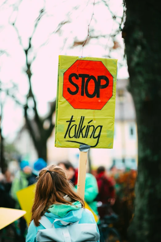 a woman holding a protest sign while standing next to a tree