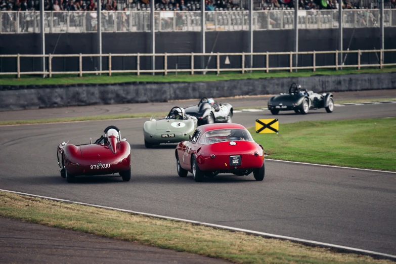 three antique cars going around a track while spectators look on