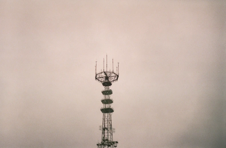 the top of a tall cellular phone tower against a cloudy sky