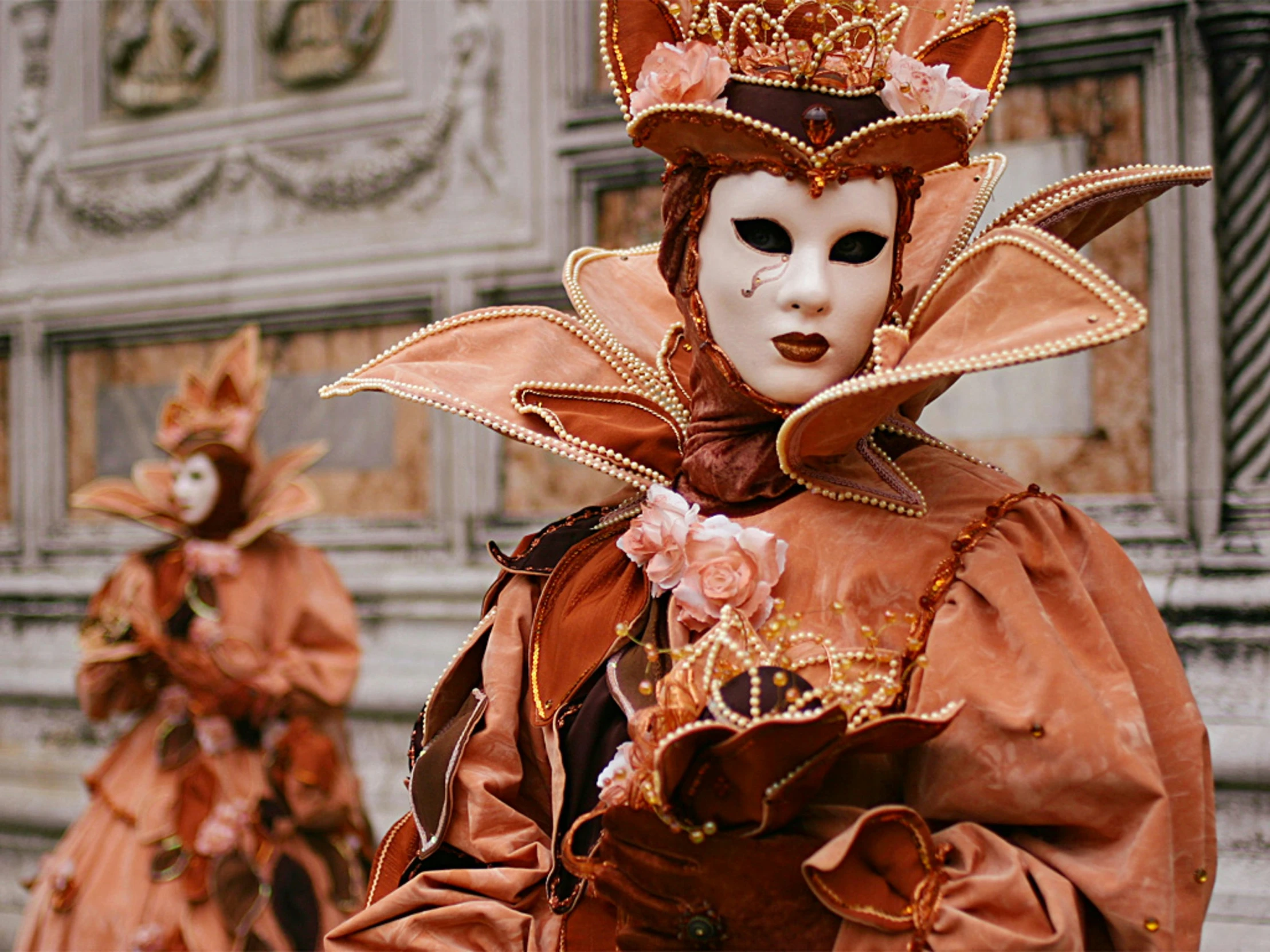 two masquerades, one with flowers, are outside in the sun