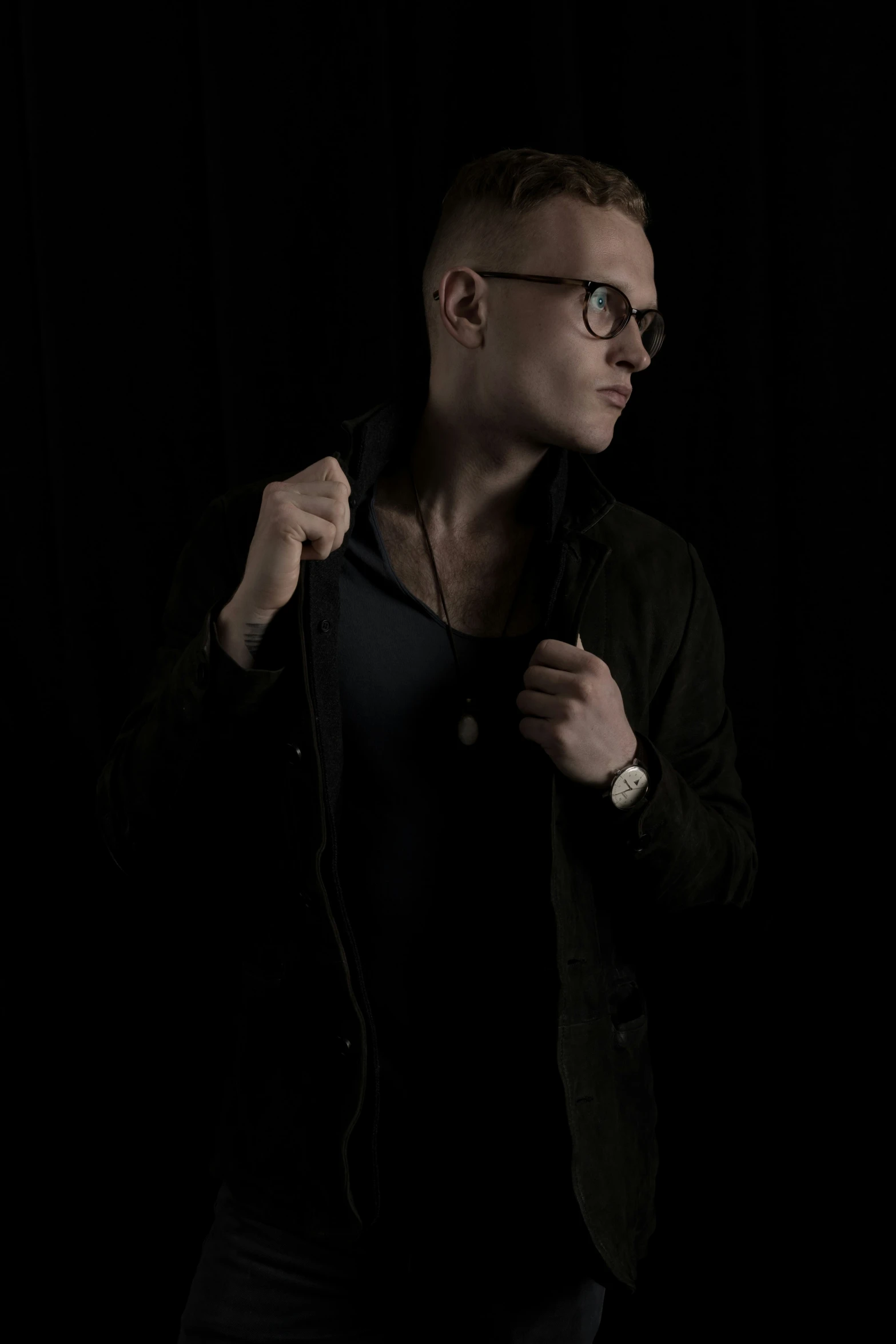 man with glasses adjusting jacket in black background