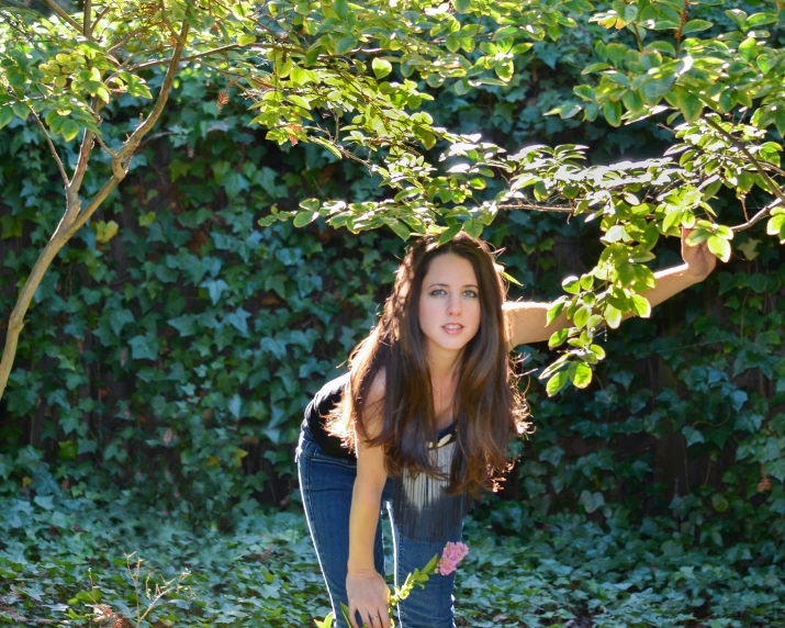 a pretty young woman holding a skateboard while leaning against a tree