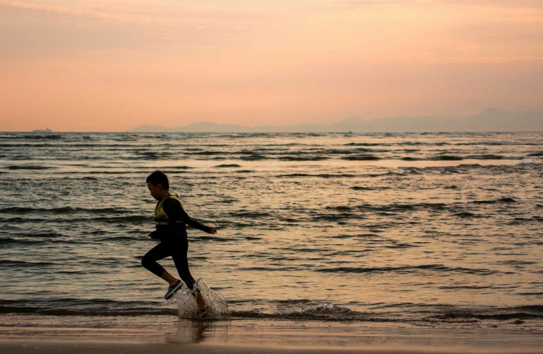 person running along the beach with a colorful sky behind them