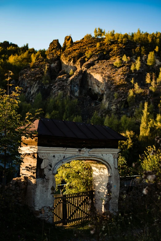 a mountain view shows trees and vegetation in the foreground with a gate to an area that contains stone structure,