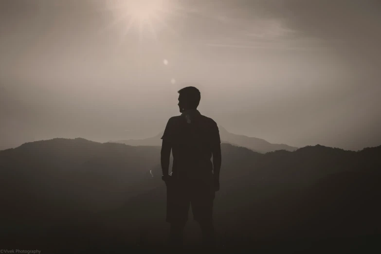 a man standing on a hill overlooking mountains with the sun shining