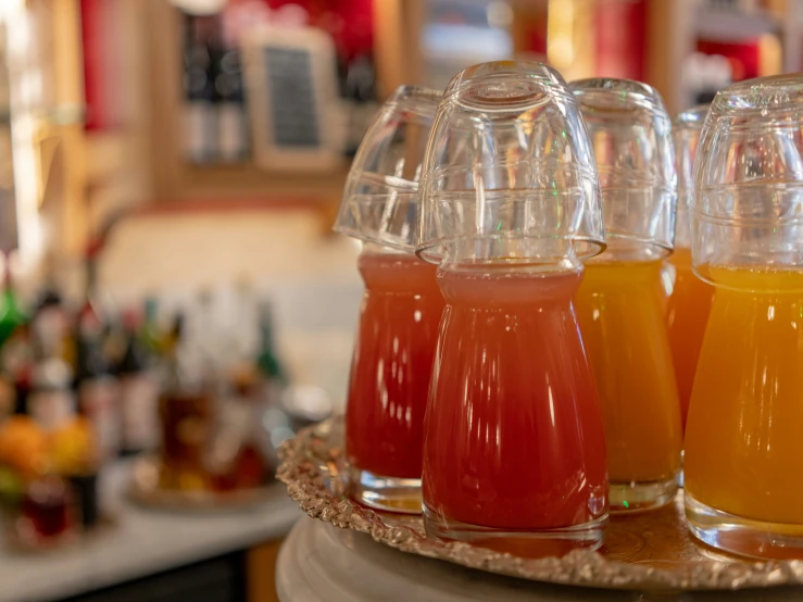 four glasses are set on a serving tray holding oranges and strawberry juice