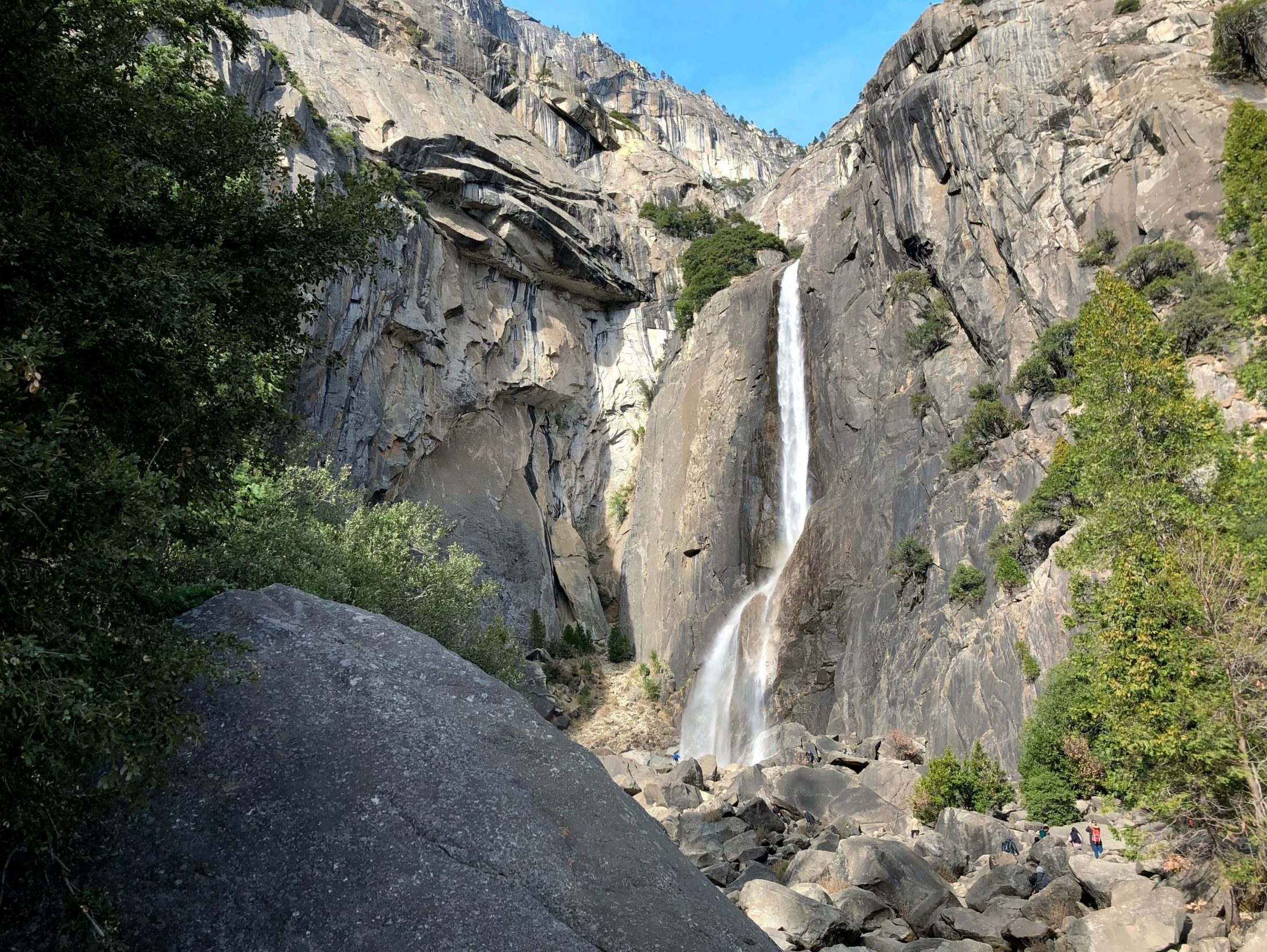 a group of people are standing near a tall waterfall