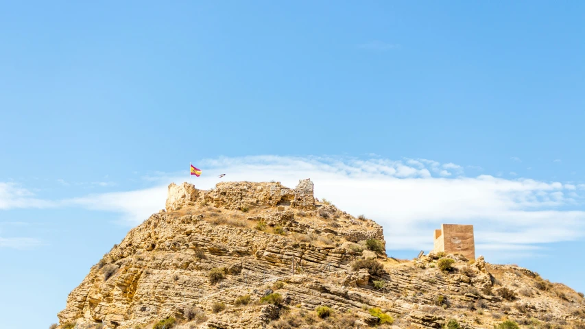 an upward view of a rocky mountain with a flag flying at the top