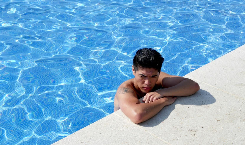 man laying by edge of swimming pool looking off into distance