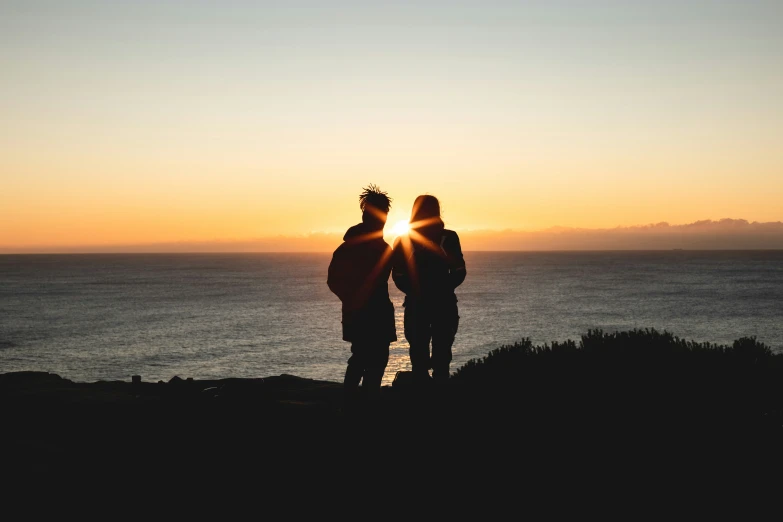 the two friends are silhouetted by the sun at sunset