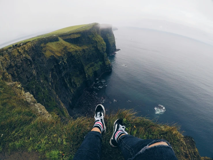 the legs of a person on a cliff overlooking water