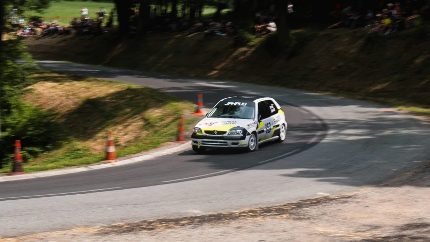 an automobile driving down a road with spectators looking on