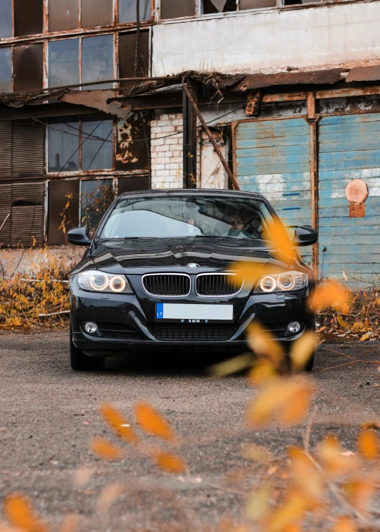 a parked black bmw in front of a rusty building