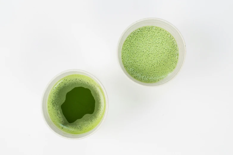 two cups filled with green colored liquid on top of a table