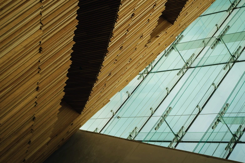 the wall of glass in front of a building that's covered in wood and is reflecting the sky