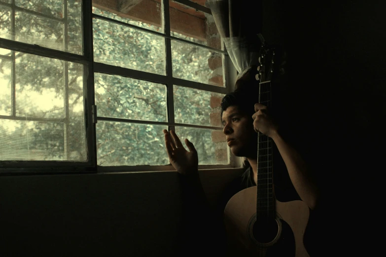 the man is holding up a guitar near a window