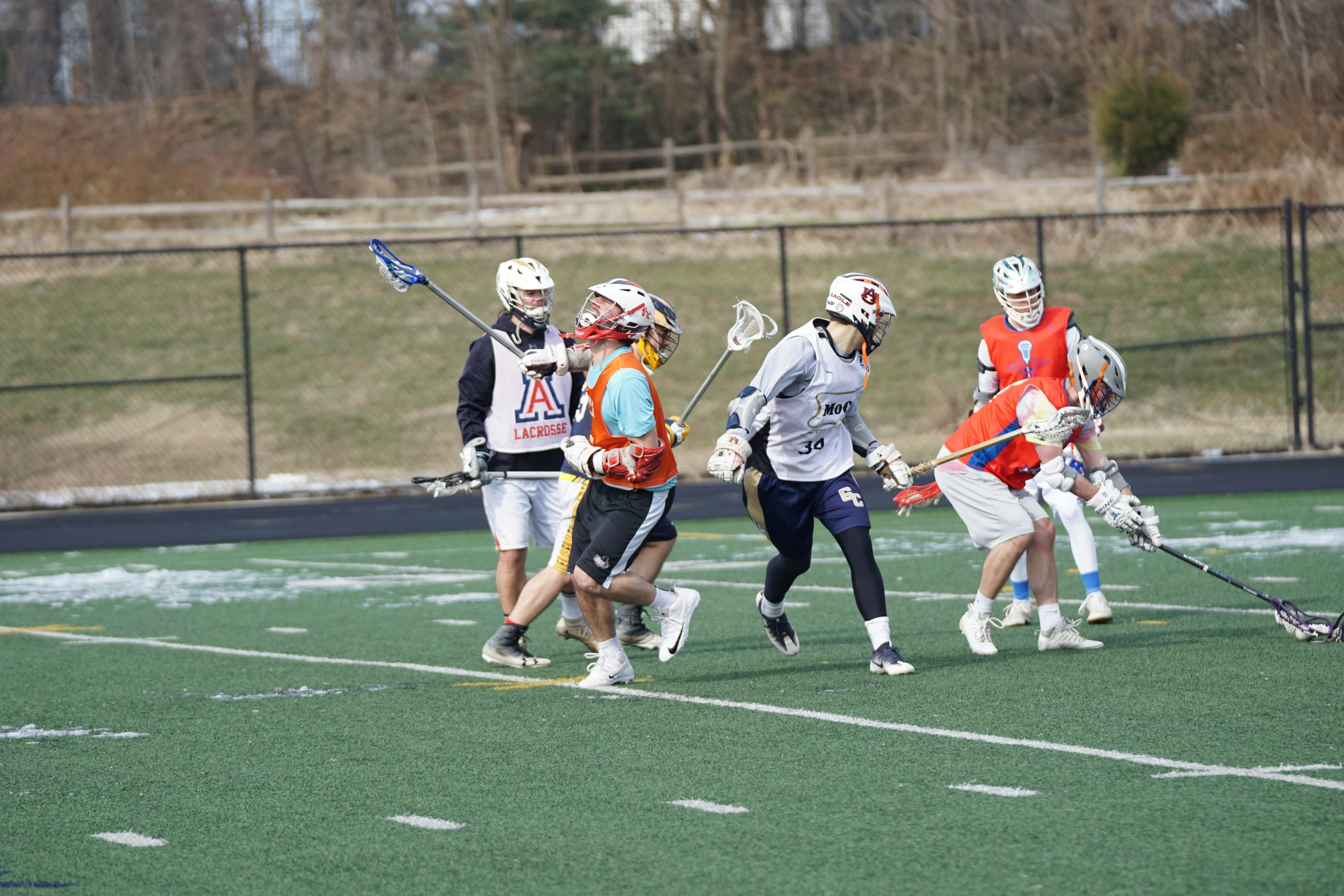 four young children play lacrosse together in front of a metal fence