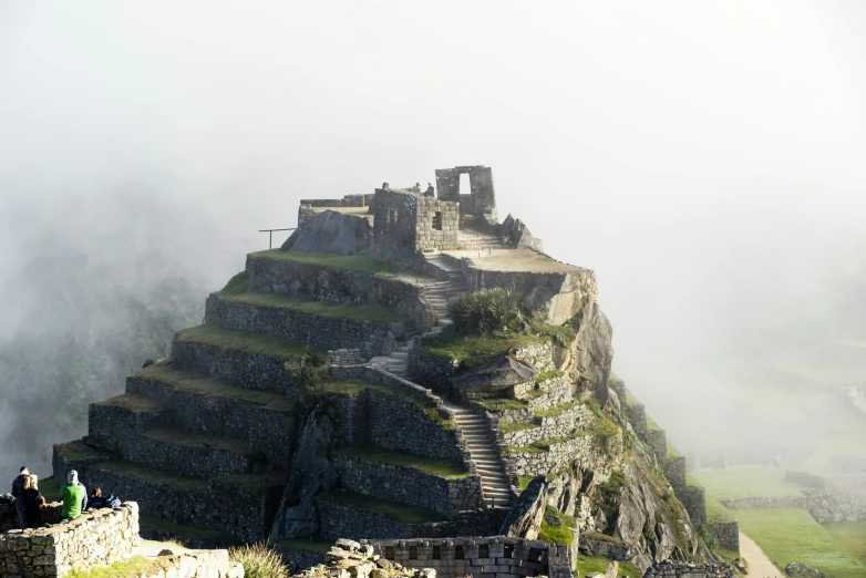 people sitting on the stairs of a large building that is made of rock