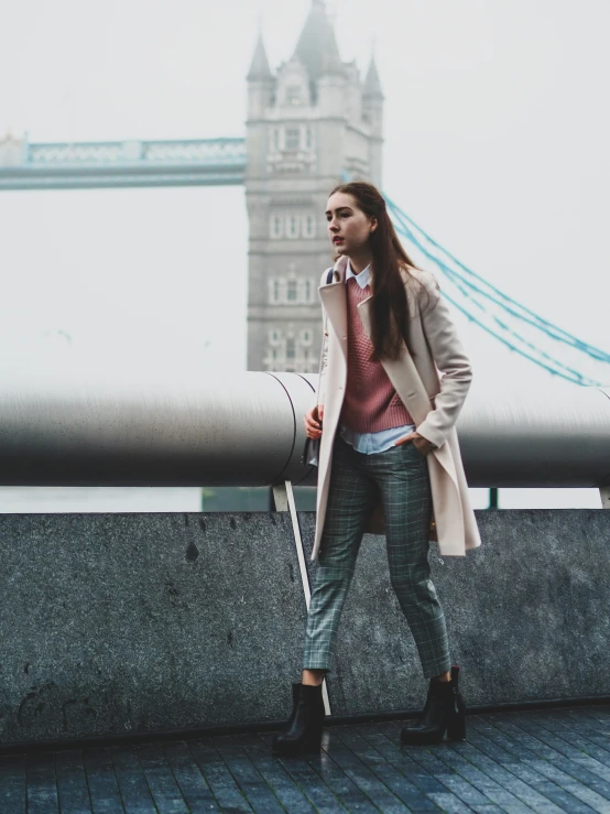 a woman in black shoes stands near a wall with a large pipe