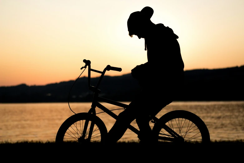 a silhouette po of a person riding a bike in front of the sunset
