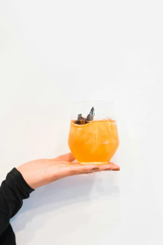a person is holding a glass with orange drink