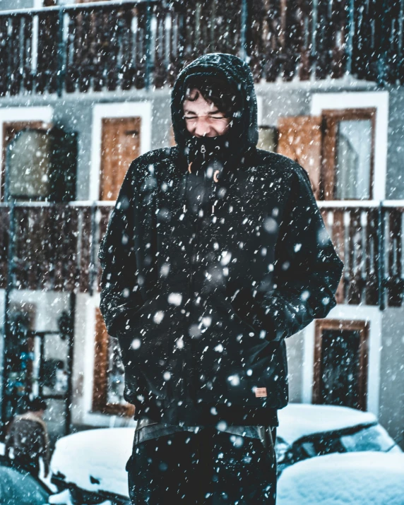 a man wearing a black coat standing on a sidewalk in front of a building in winter